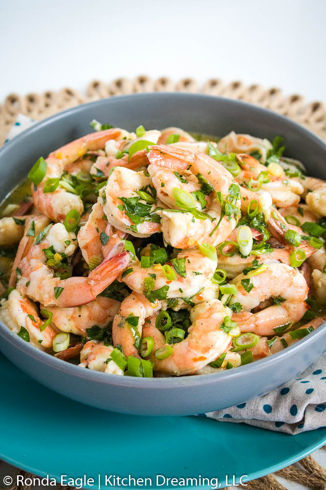 A blue bowl filled with shrimp that have been pickled in an herb vinaigrette.