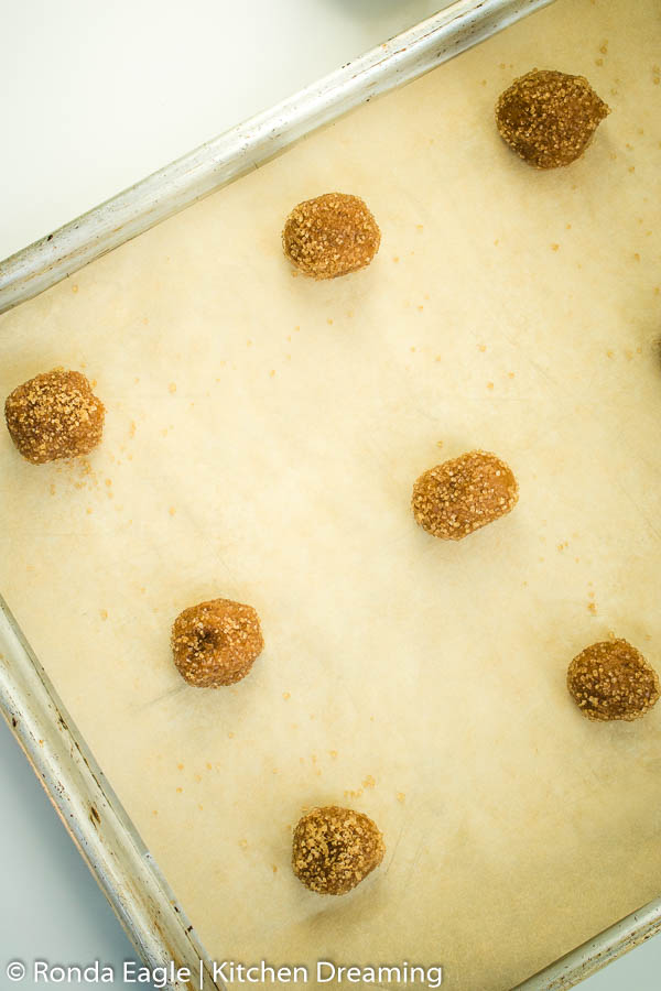 Raw Molasses Cookie dough rolled into 1-inch balls on a rimmed baking sheet fitted with a sheet of parchment paper.