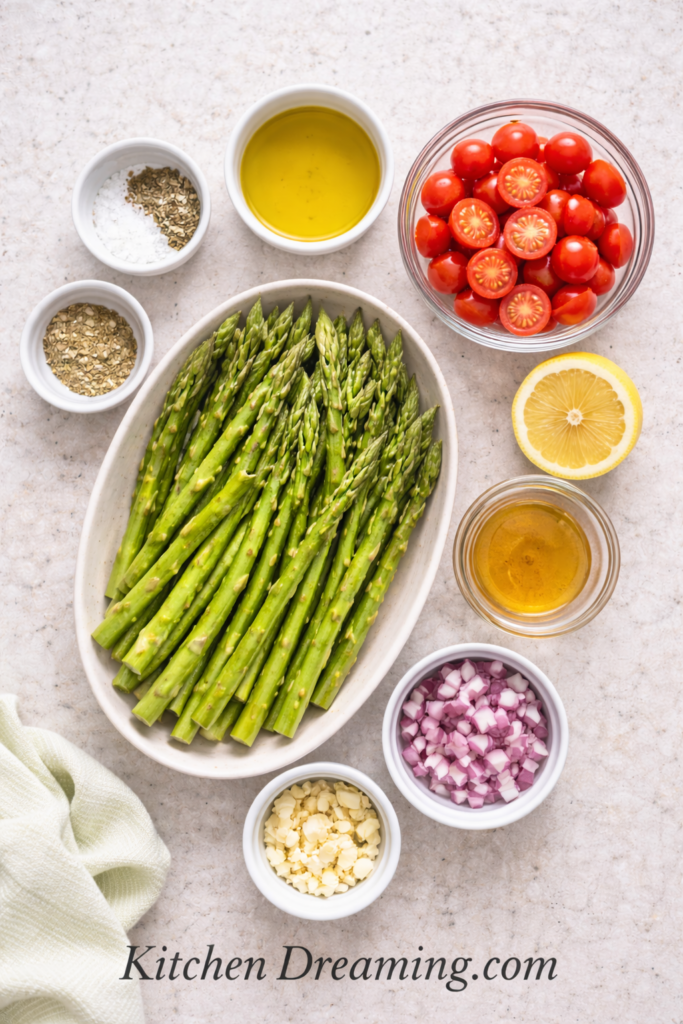 Asparagus Salad Recipe (Easy Fresh Spring Side Dish) 3 Flat lay of ingredients for raw asparagus salad recipe including asparagus, tomatoes, red onion, lemon, and olive oil.