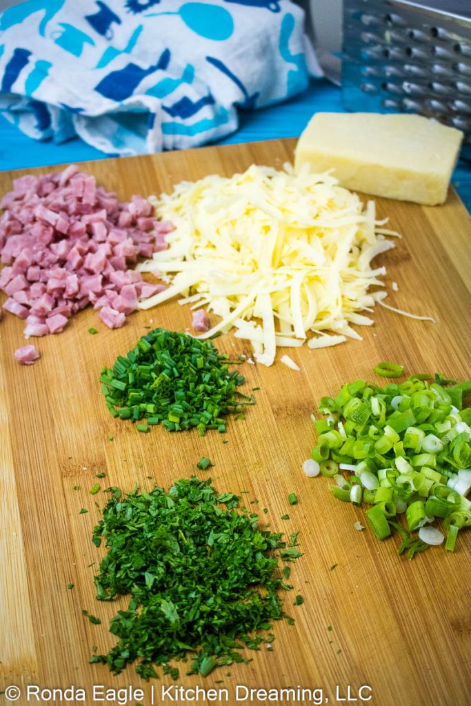 The ingredients for ham and cheese scones: freh herbs, cheese, ham on a cutting board.
