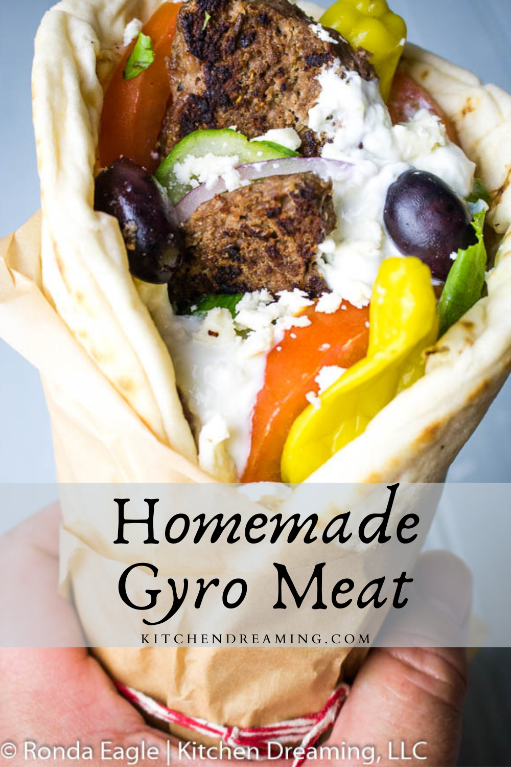 A pinnable image of Greek Gyro meat wrapped in a soft pita layered with lettuce, tomatoes, cucumbers, onions, olives, pepperoncini peppers, tzatziki sauce, and crumbled feta cheese. 