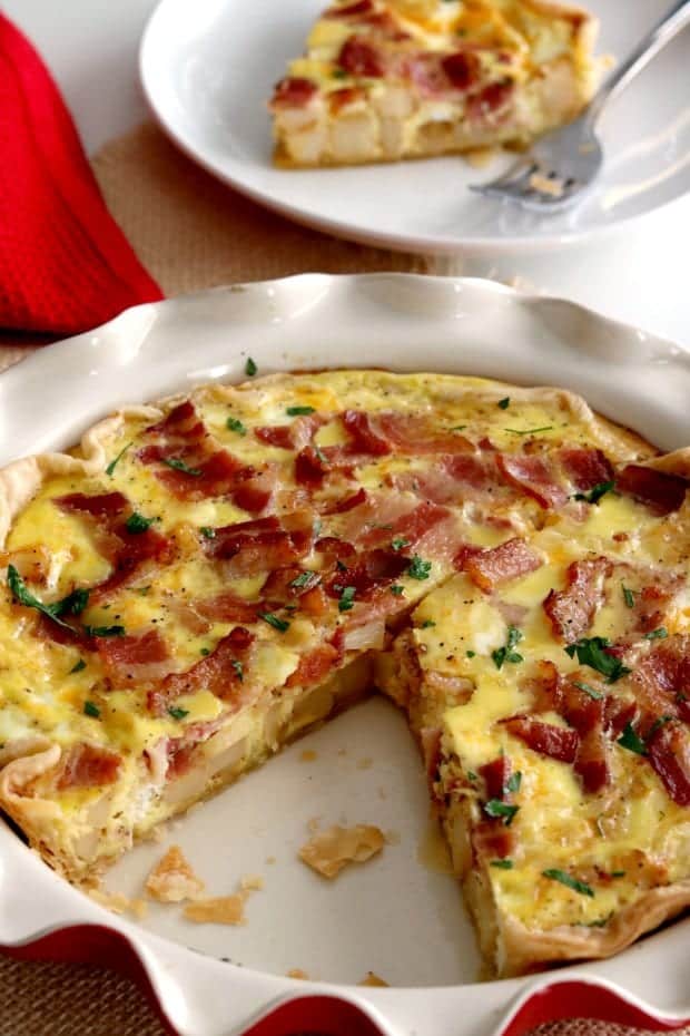 An image of a bacon and potato quiche with a slice removed. 