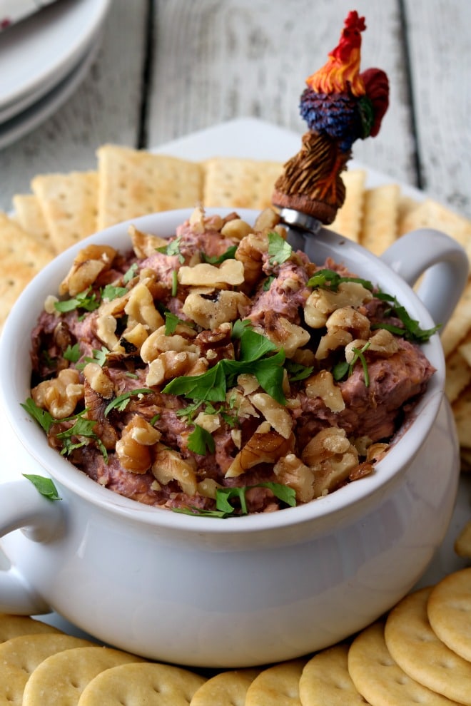 A bowl of port cheese spread sprinkled with parsley and toasted walnuts surrounded by crackers.