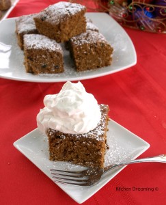 Gingerbread cake on a plate with whipped cream and a dusting of powdered sugar.
