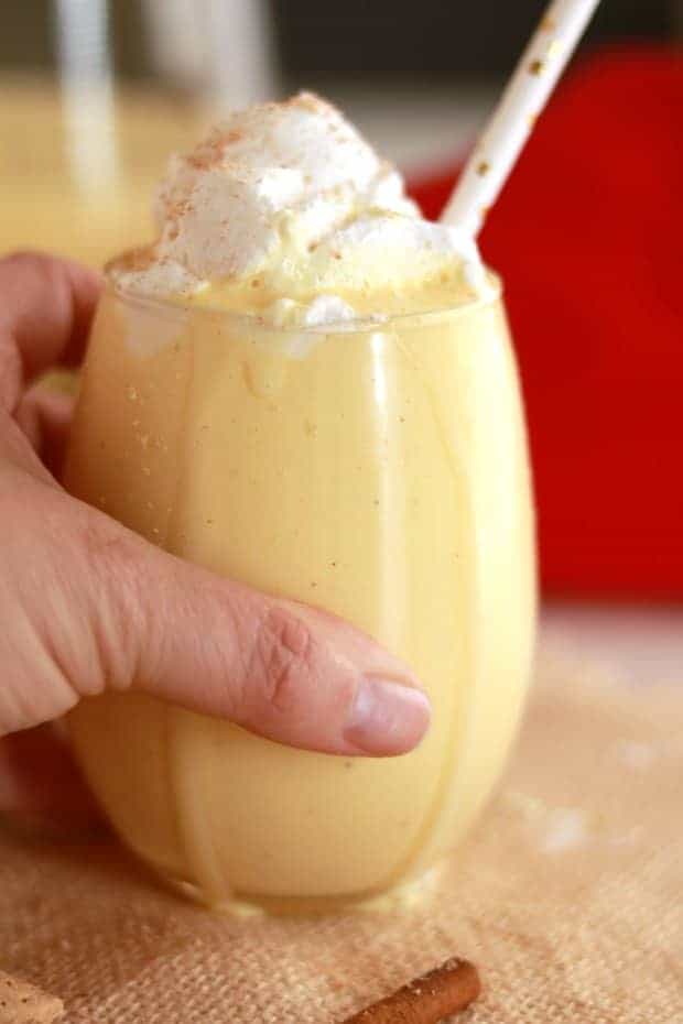 an up close shot of a glass of eggnogg topped with whipped cream and nutmeg.