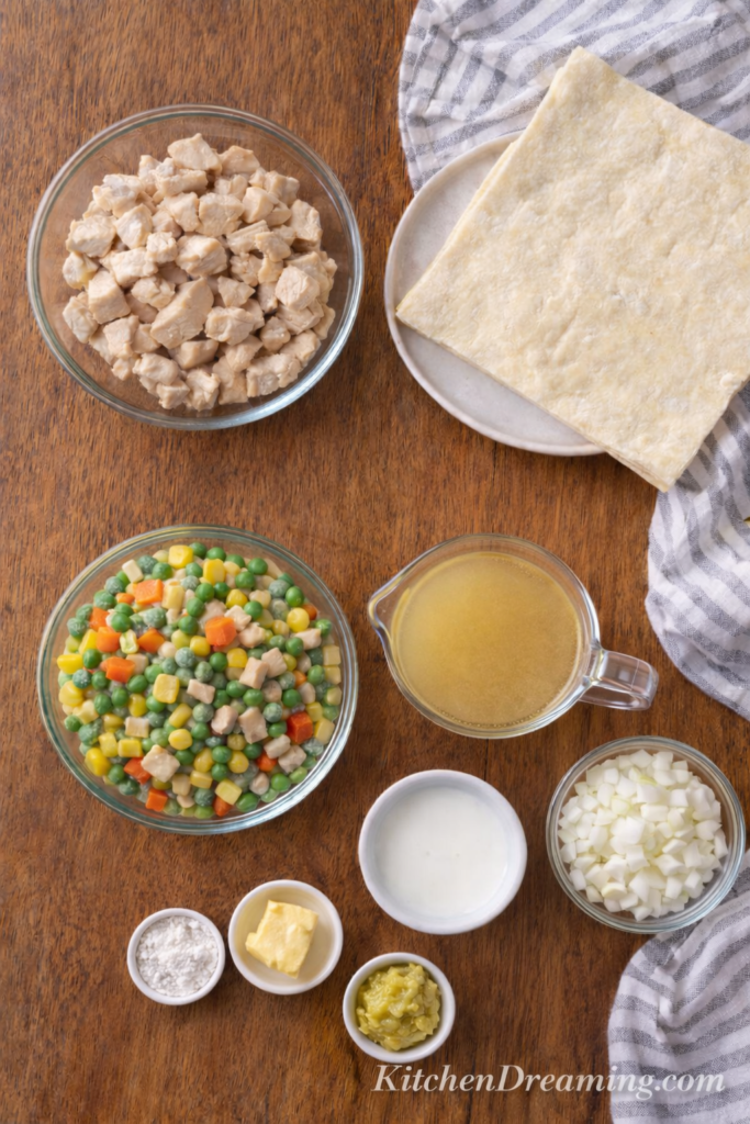 Chicken Pot Pie Casserole (Easy Creamy Comfort Bake) 3 Overhead ingredient flat lay for chicken pot pie with puff pastry including chicken, onions, vegetables, stock, milk, flour, butter, bouillon paste, and puff pastry.