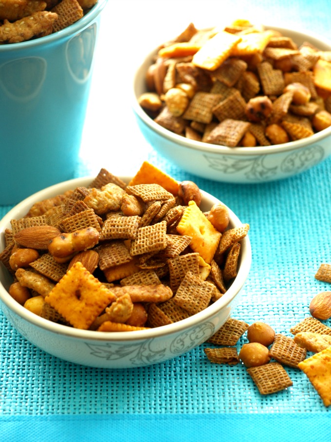 three small bowls of spicy homemade chex mix on a blue back ground.