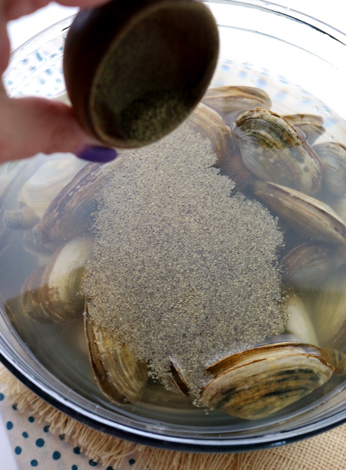 An image of how to clean clams. Clams are in a bowl of water and ground black pepper is being added. 