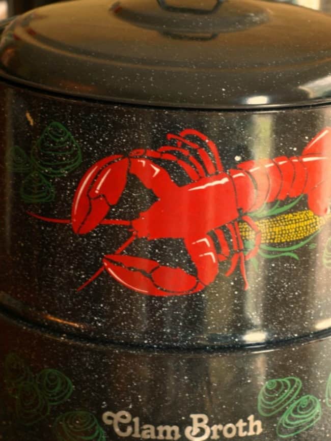 An image of a traditional New England style clam and lobster pot. It has two sections, a bottom pan where you add the water and it collects the juices. In this bottom portion is a faucet for dispensing broth. The top pot is fitted to the bottom pan and has holes in the bottom to allow the food to steam. The whole assembly has a lid for keeping the steam inside.