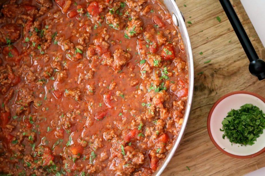 A pan of American goulash sauce consisting of tomato, sauce, fire roasted tomatoes, ground beef and fresh herbs on sitting on a wooden board.