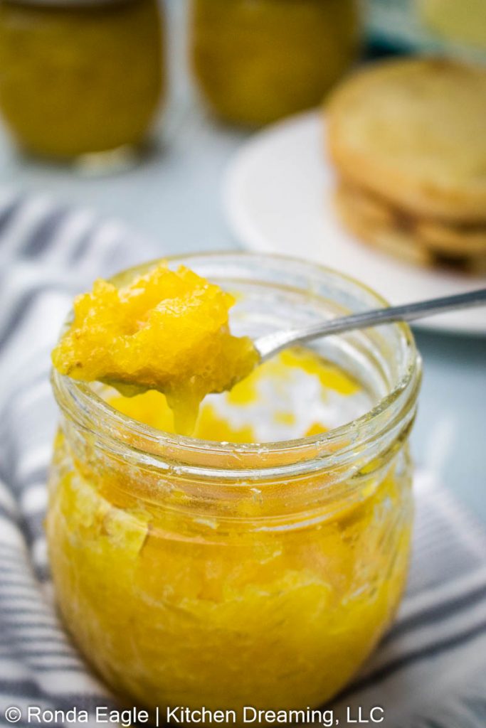 A close-up image of a jar of fresh pineapple jam. A spoonful of jam rests across the top of the jar revealing the bright-yellow jam.. 
