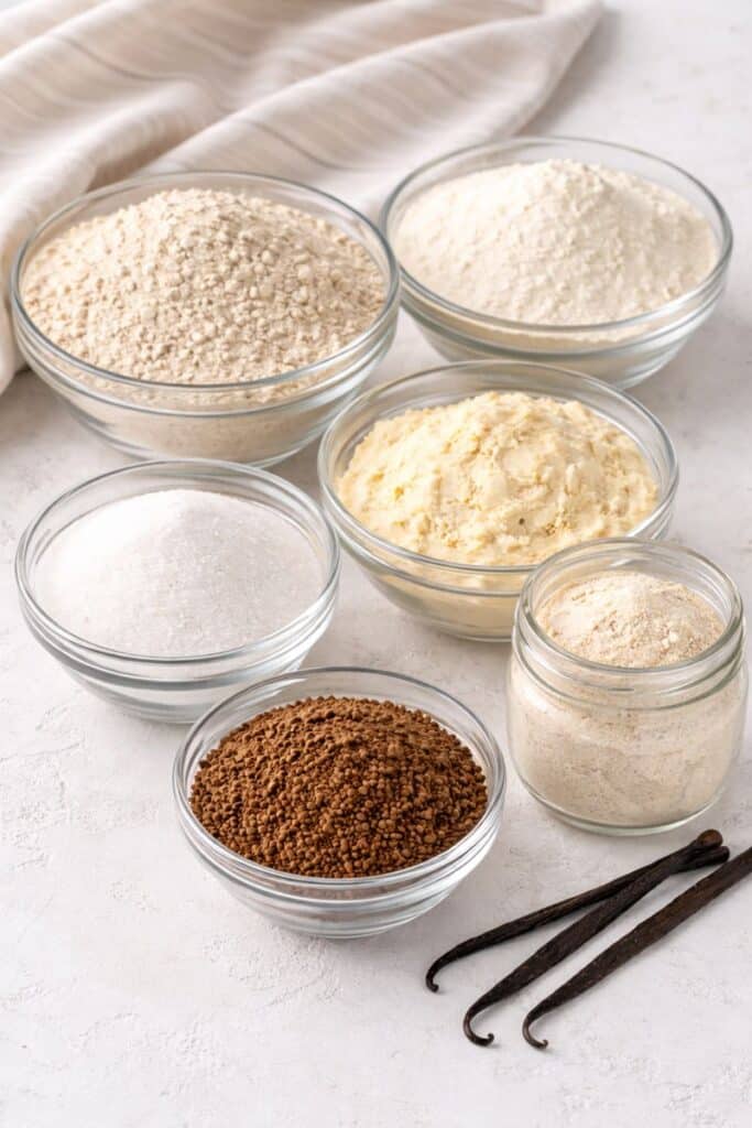 Bowls of dry milk powder, French vanilla creamer, sugar, instant coffee granules, and vanilla pudding mix for homemade instant vanilla latte mix.