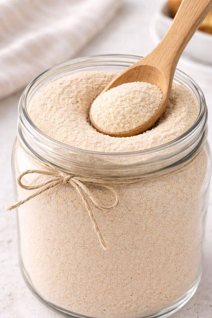 Close-up of homemade instant vanilla latte mix powder texture in a glass jar with a wooden scoop.