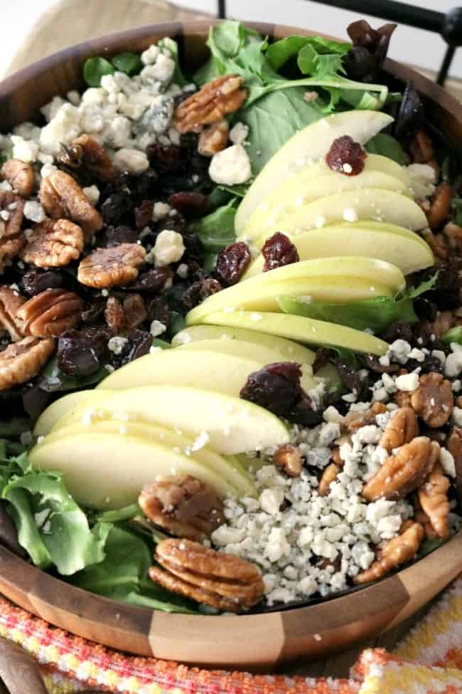 A 3/4 angle shot of Apple Pecan Blue Cheese Salad with Apple Vinaigrette in a wooden bowl.