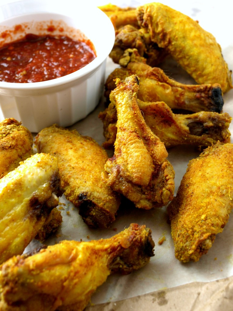 Baked curry wings on parchment paper with hot dipping sauce.