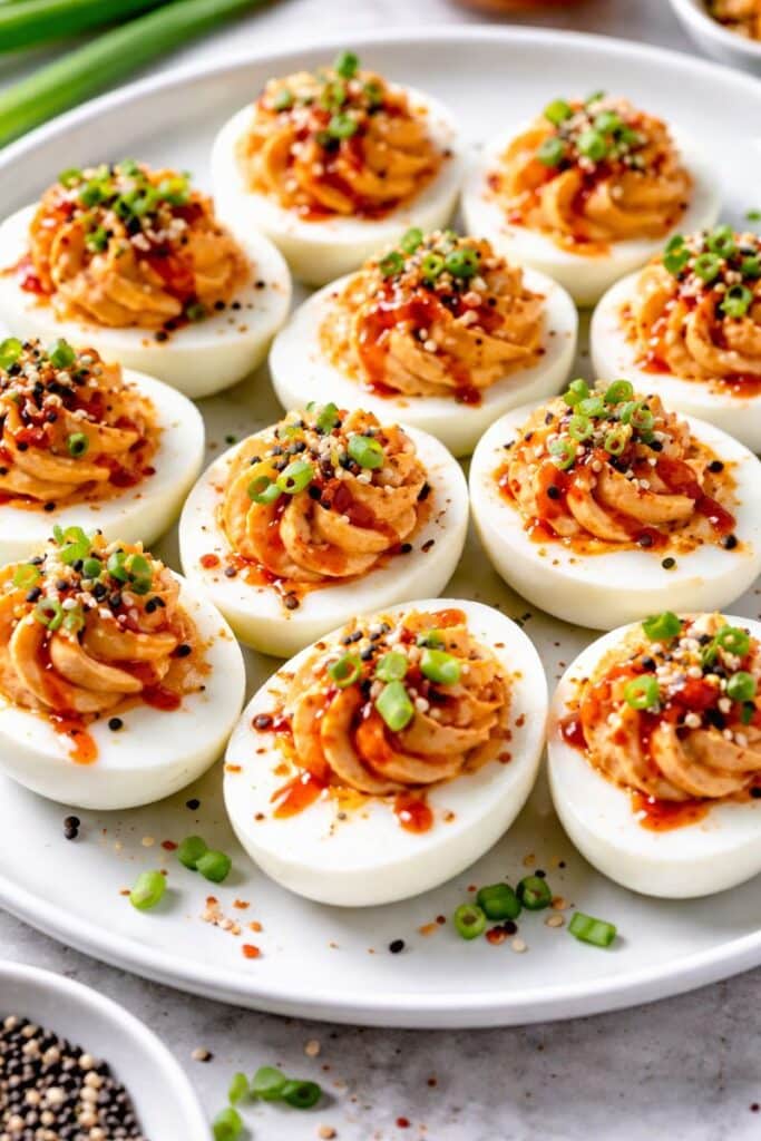 Asian-inspired spicy sriracha deviled eggs topped with sesame seeds and green onions on a serving platter.