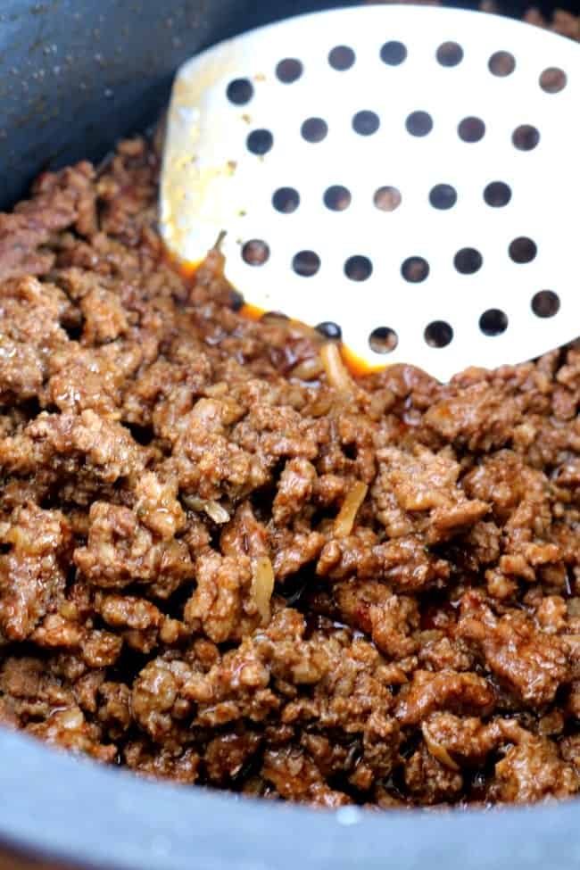 Ground Beef seasoned with taco seasoning in the slow cooker insert with a slotted spoon. 