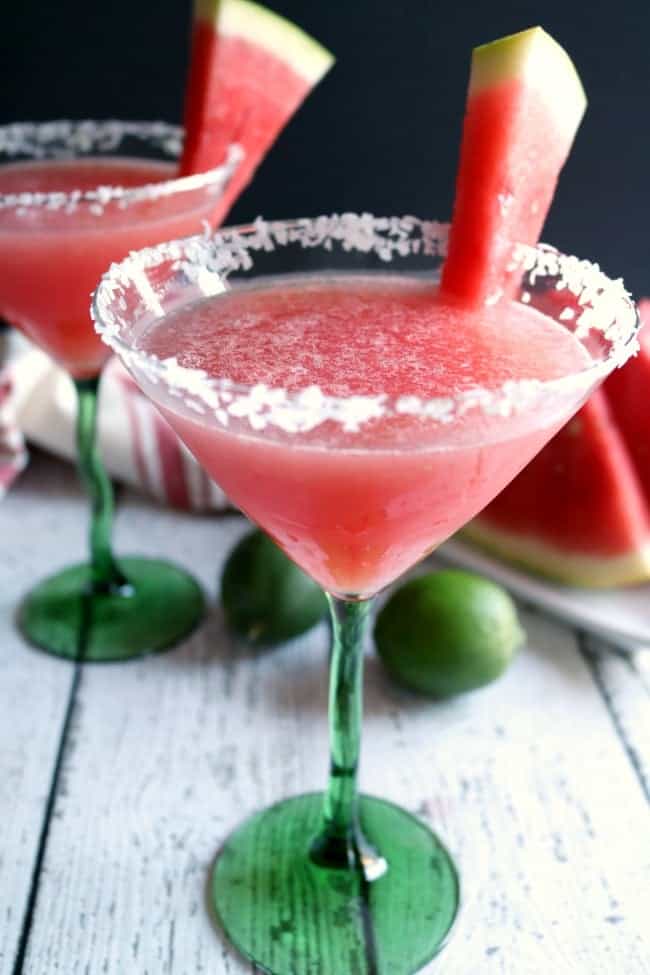 two watermelon margaritas served with a salted rim and a wedge of watermelon.