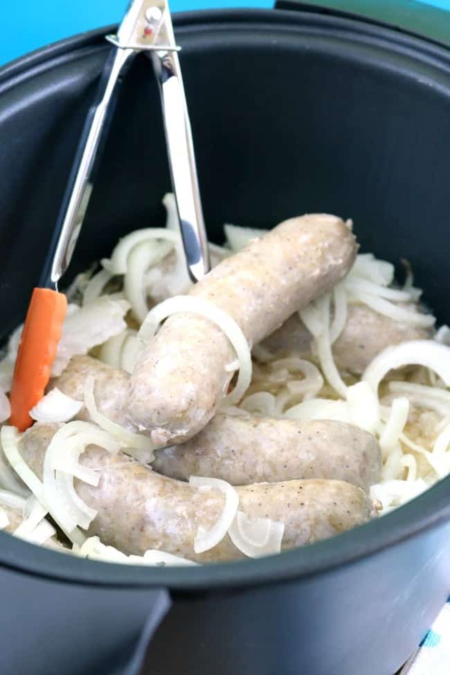A crock pot filled with brats, onions and sauerkraut.