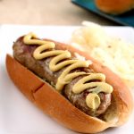 A grilled bratwurst in a soft bun topped with a zig-zag of spicy brown mustard.