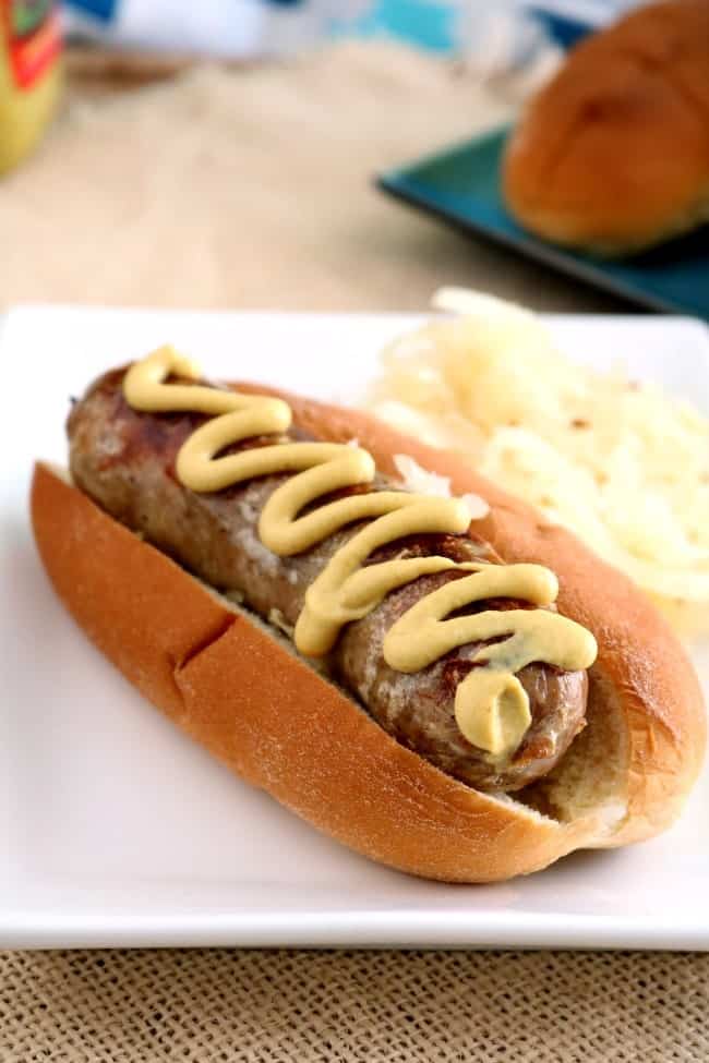 A grilled brat on a bun with a zig-zag of spicy brown mustard
