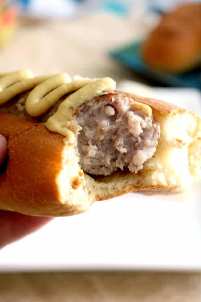 an up-close photo of a bratwurst in a bun with spicey brown mustard; a bite has been taken.