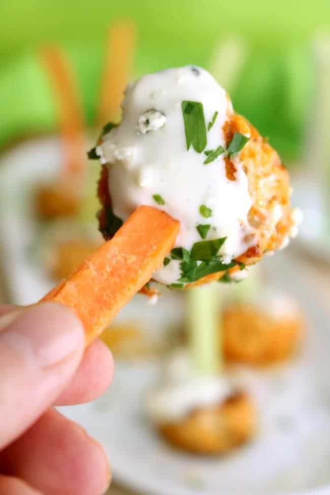 A baked buffalo chicken meatball on a carrot stick for a portable party snack.