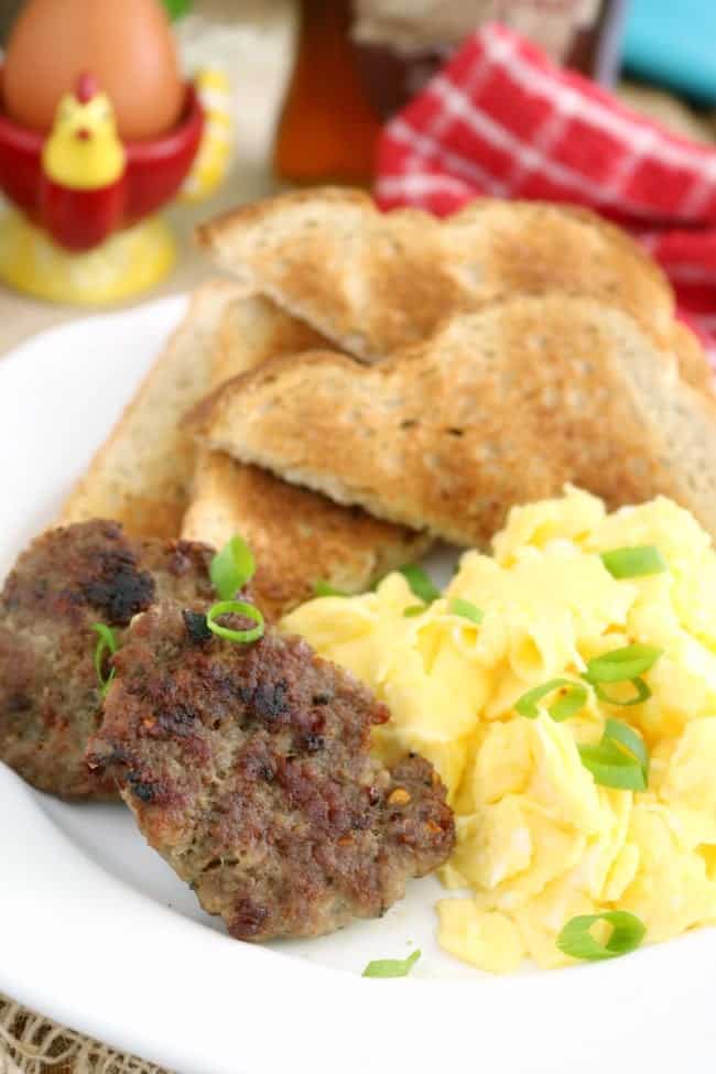 a plate of scrambled eggs, two slices buttered toast, and two homemade breakfast sausage patties