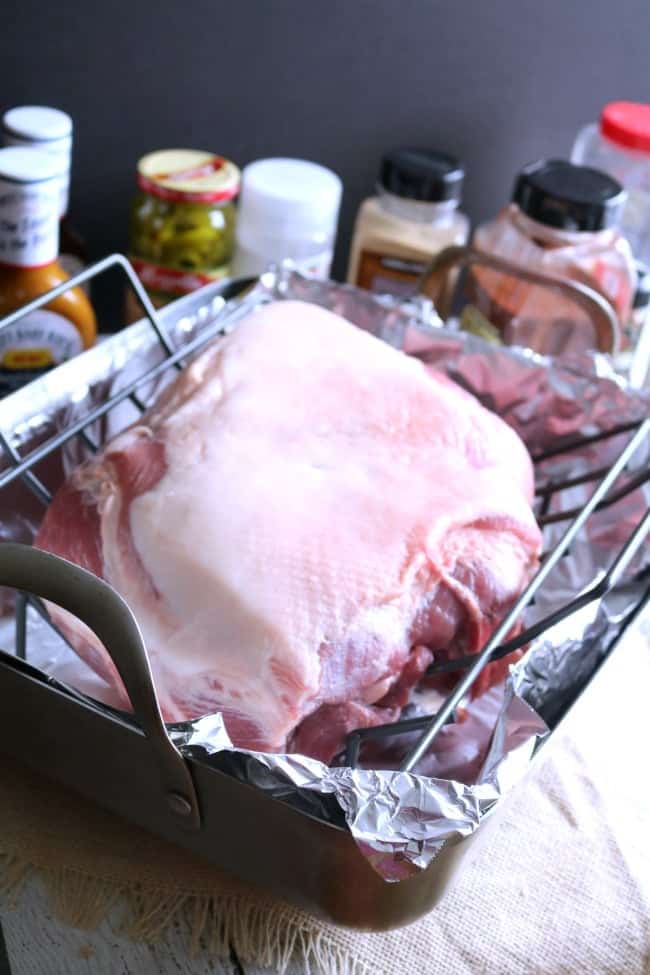 A roasting pan with a trimmed pork butt on a roasting rack ready to head into the oven.
