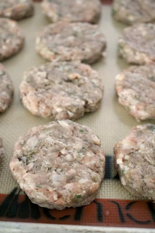 an in-process image of pressed sausage patties on a silicon lined tray ready to be flash-frozen.