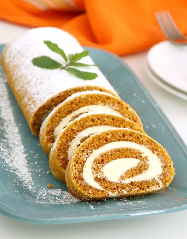 An image of a plate of pumpkin cake roll that is sliced to serve. It is garnished with a sprig of holly.