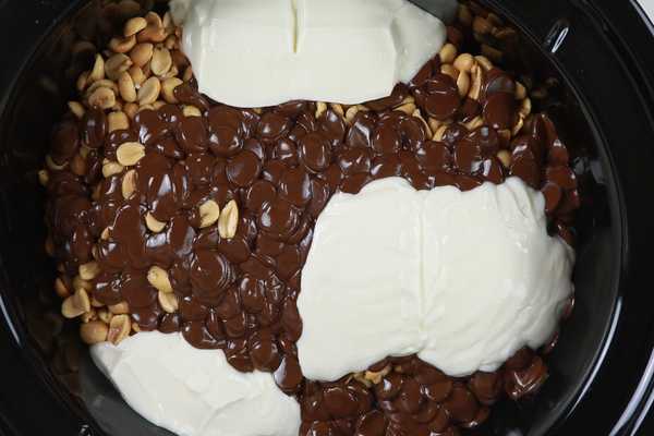 A crock pot filled with peanuts, bittersweet dark chocolate and almond bark ready to be stirred into chocolate peanut clusters