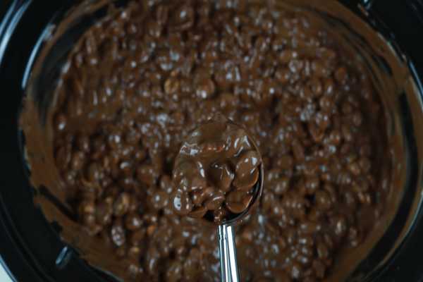 A slow cooker of easy chocolate peanut clusters and a scoop filled with chocolate and peanuts