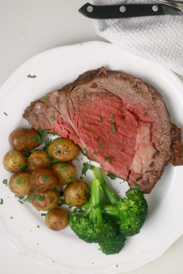 sliced prime rib on a plate with roasted potatoes and steamed broccoli.