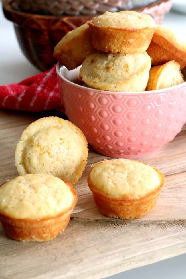 Cornbread muffins on a wooden board and stacked in a small pink bowl.