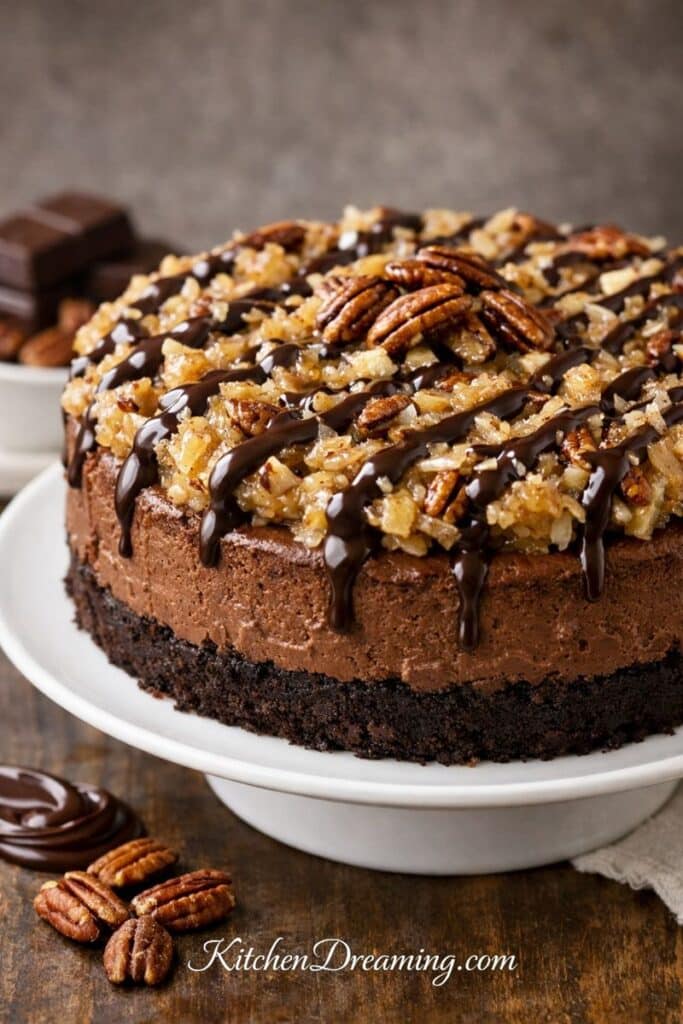 German chocolate cheesecake recipe with homemade coconut-pecan topping and chocolate drizzle, served on a cake stand.