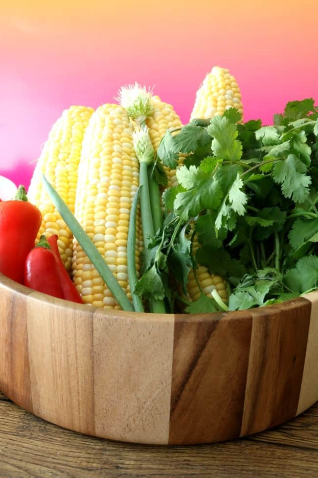 A wooden bowl filled with fresh corn, red jalapenos, green onions and cilantro.