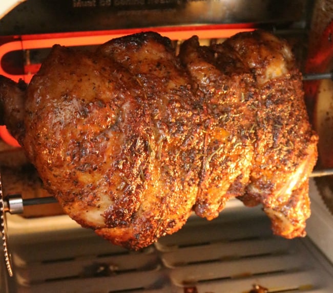 An image of a boneless leg of lamb cooking on the spit in an electric rotisserie oven. 