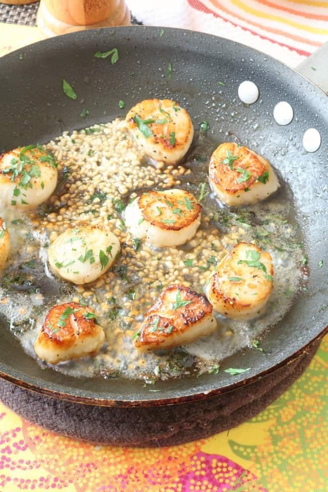 Scallops in a skillet with garlic and butter.