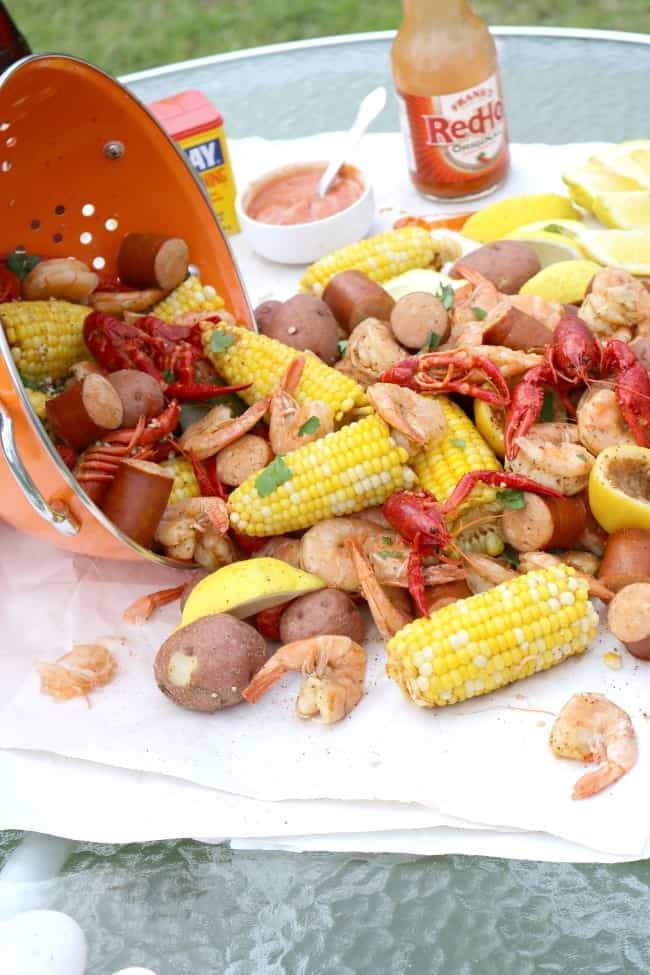 A side view of a lowcountry crawfish boil laid out on a picnic table with fresh corn, keilbasa, andouille sausage, shrimp, and crawfish.