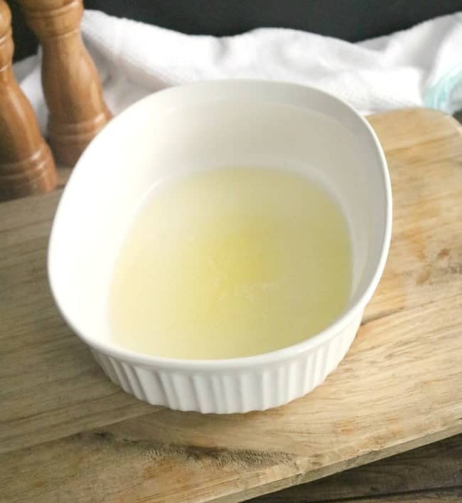 A casserole dish with a stick of melted butter on a wooden cutting board