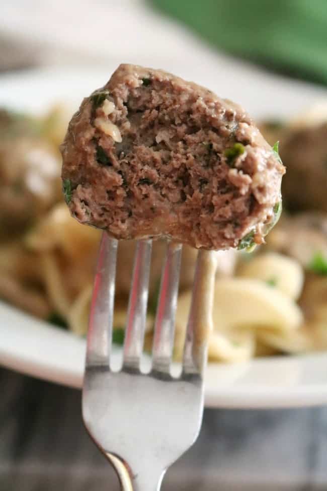 A meatball on a fork with a bite taken out of it. The interior of the meatball reveals herbs and spices. 