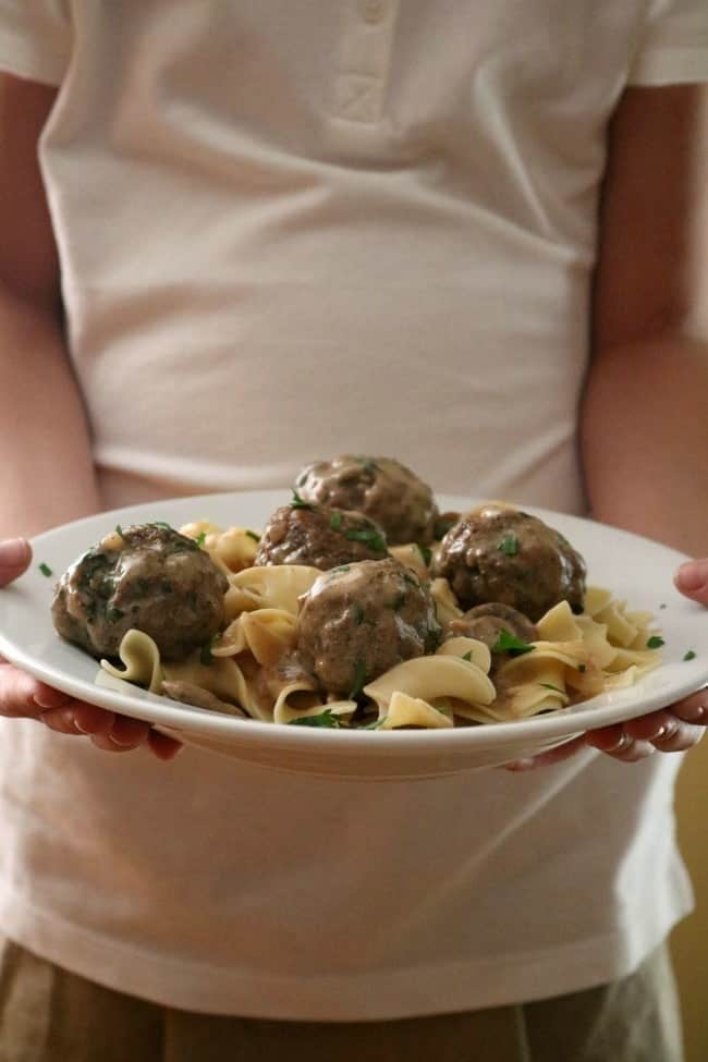 A person holding a plate of meatball stroganoff on a bed of buttered egg noodles.
