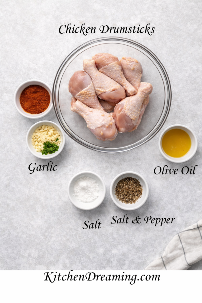 Baked Garlic Paprika Chicken (No Fail Juicy Oven Method) 3 Ingredient flat lay labeled chicken drumsticks, paprika, garlic, olive oil, salt, and pepper for baked garlic paprika chicken.