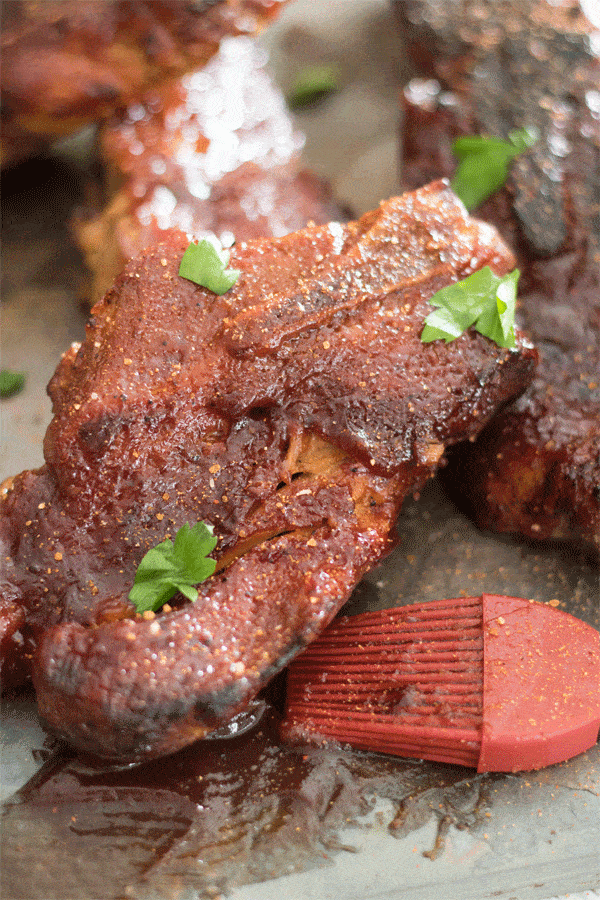 A close-up photo of Instant Pot Country Pork Ribs in a dark slate tile. A pastry brush covered with BBQ sauce sits in the foreground.