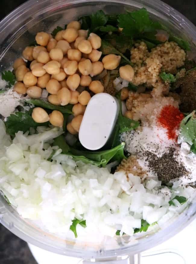 an overhead shot of the ingredients for air fryer falafel in a food processor: chick peas, minced garlicm salt, onions, black pepper, and parsley getting ready to be ground to for the raw falafel mix.