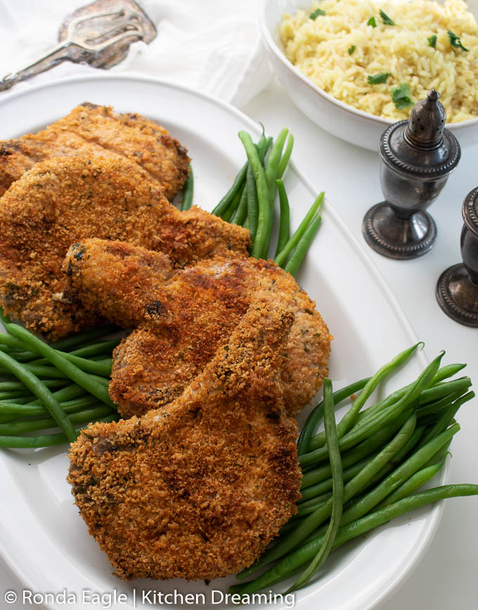 A serving plate filled with crispy air fryer pork chops which have been breaded and cooked to a perfect golden brown. 