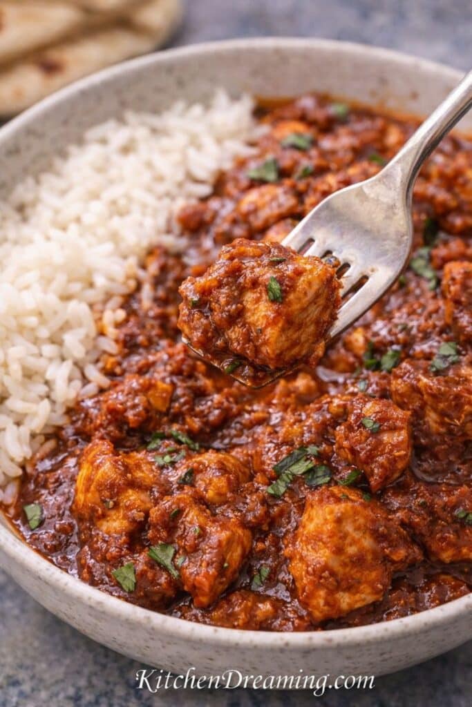 Easy chicken vindaloo recipe close-up with a fork bite, showing tender chicken coated in a tangy, spicy Indian curry sauce.