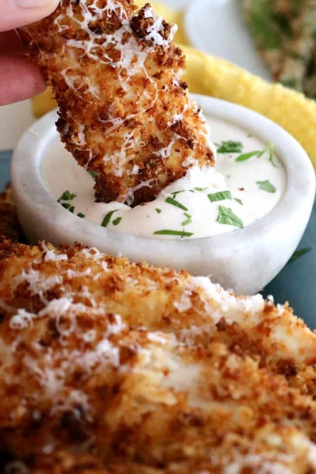 A close-up photo of an air fried garlic Parmesan chicken tender being dunked into ranch dressing.