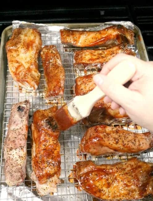 A tray of oven baked Country-Style Pork Ribs is being brushed with the initial application of BBQ sauce.